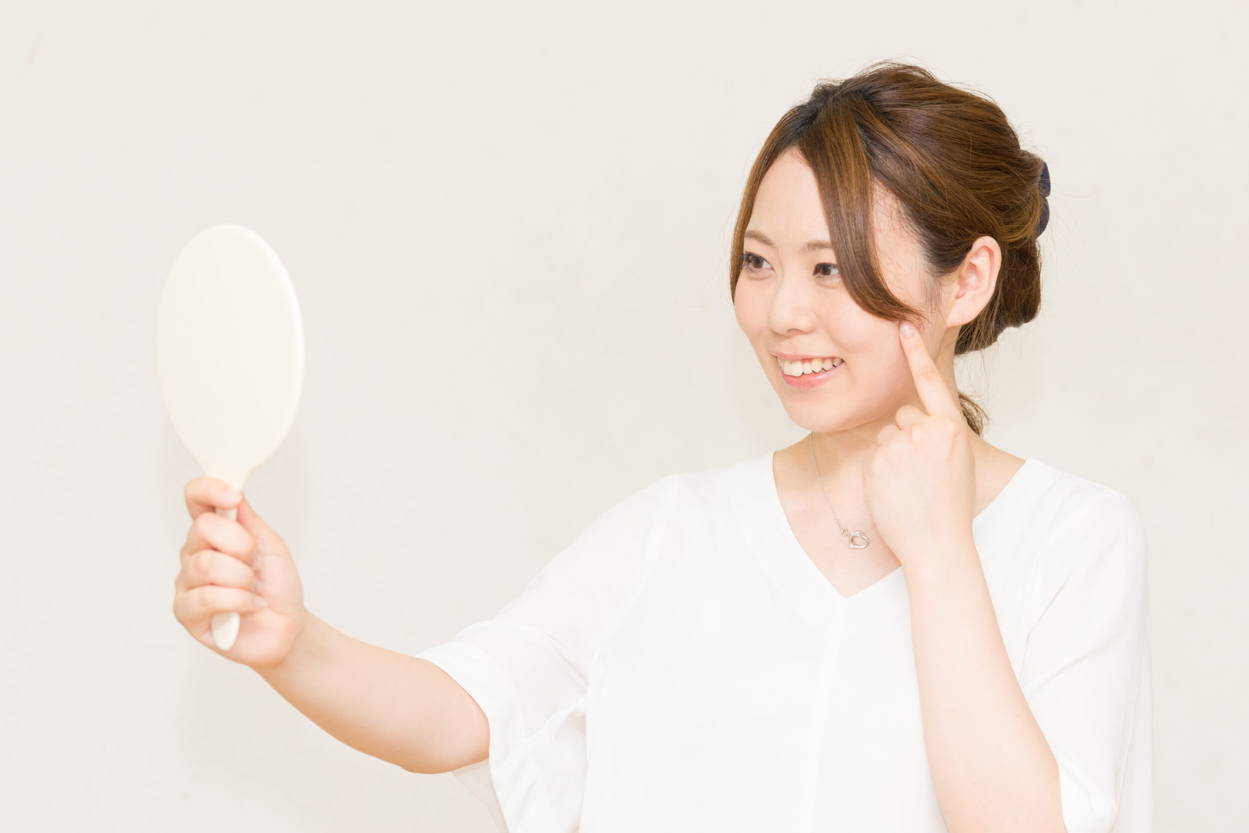 Woman smiles in the mirror after a facelift, touching her cheek with one finger