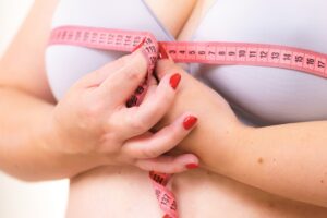 Woman with large breasts holds tape measure around her chest and thinks of breast reduction benefits