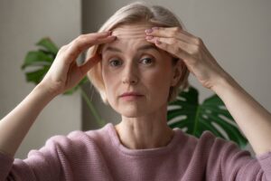 A mature woman holds her wrinkled forehead, contemplating plastic surgery